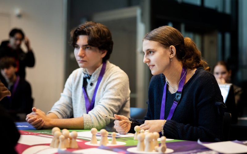 Eine Schülerin und ein Schüler sitzen vor dem ECOMANIA Spielbrett