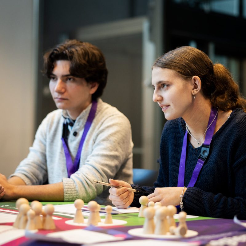 Eine Schülerin und ein Schüler sitzen vor dem ECOMANIA Spielbrett